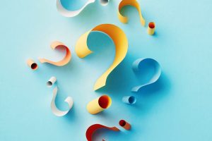 Yellow question mark surrounded by colorful question marks over blue background. Horizontal composition with copy space.